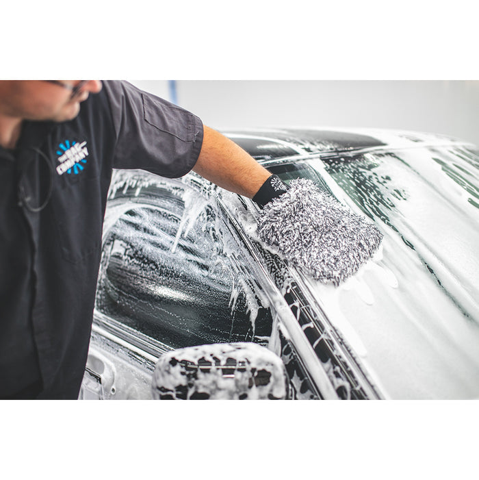 Black and white microfiber wash mitt being used to wipe down a foamy window
