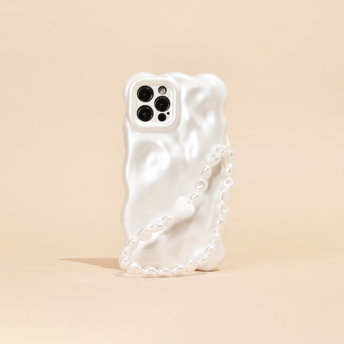 A white, wavy-textured phone case is shown standing on a light beige surface, featuring Coconut Lane's Beaded Phone Strap - Chunky Pearls. The phone's camera section with multiple lenses is visible, contributing to a sleek and modern aesthetic.