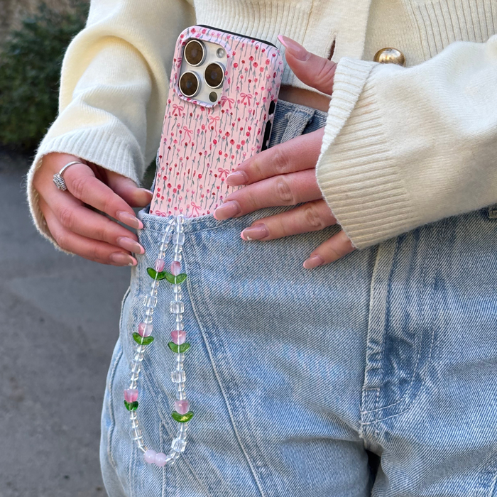 A phone with a colorful beaded tulip phone strap is being slipped into light-wash jeans.