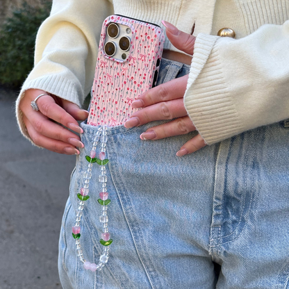 A phone with a colorful beaded tulip phone strap is being slipped into light-wash jeans.