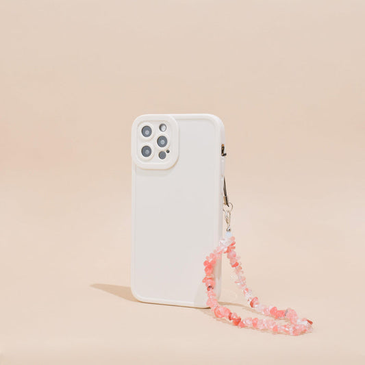 White phone case with a pink beaded Coral Crystal phone strap, standing upright on a beige background.