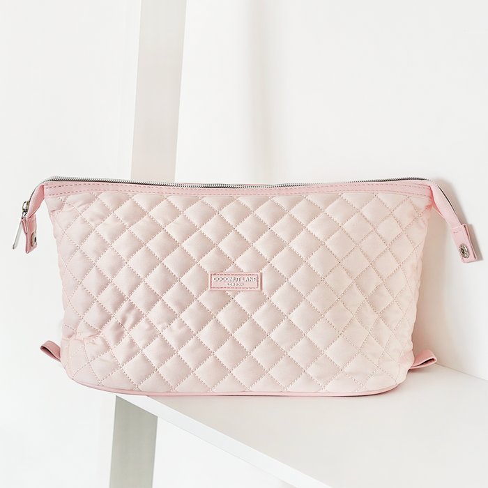 Quilted marshmallow pink expandable makeup bag with silver zipper, sitting on a white shelf.