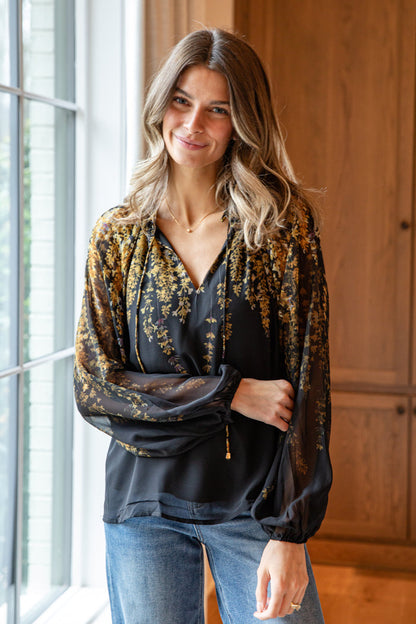 Woman wearing a floral blouse and jeans standing indoors.