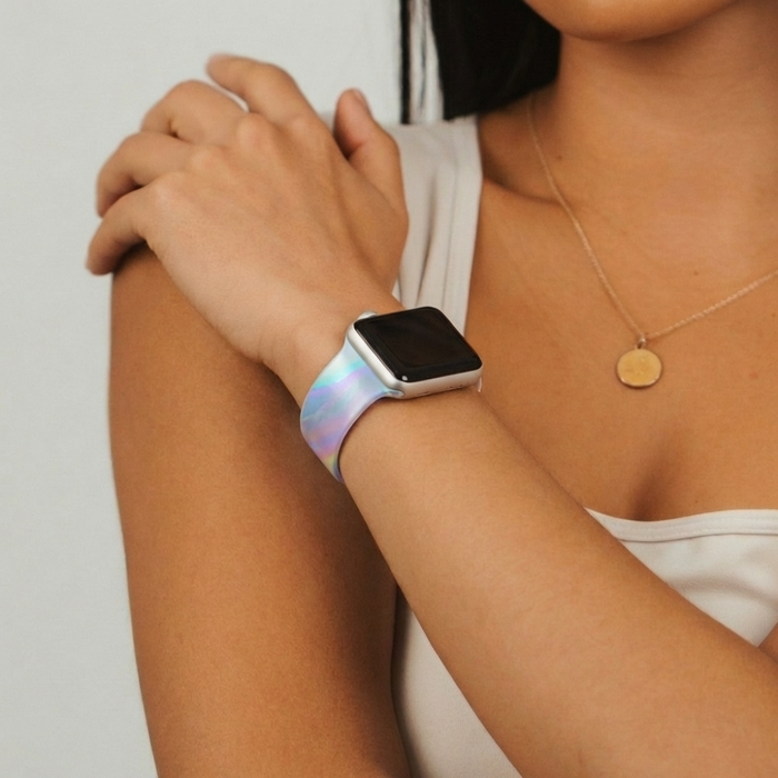 Woman wearing a holographic bubble-patterned Apple Watch strap and a gold pendant necklace, arms crossed.