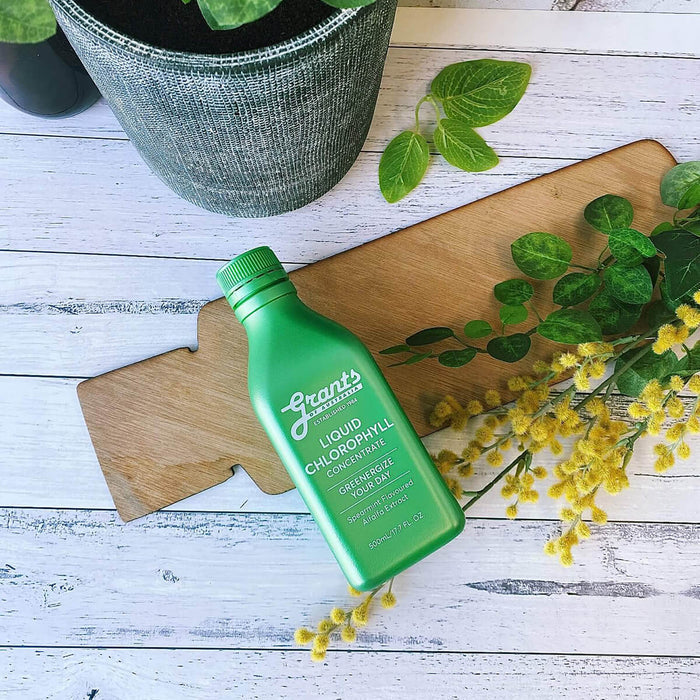 Green bottle of Liquid Chlorophyll on a wooden board with leaves and flowers.