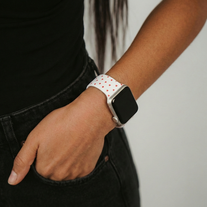White silicone Apple Watch band with red hearts, worn with a black outfit.