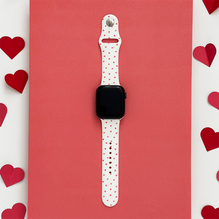 Coconut Lane Apple Watch strap with red mini hearts pattern, displayed on a red background with paper heart shapes.