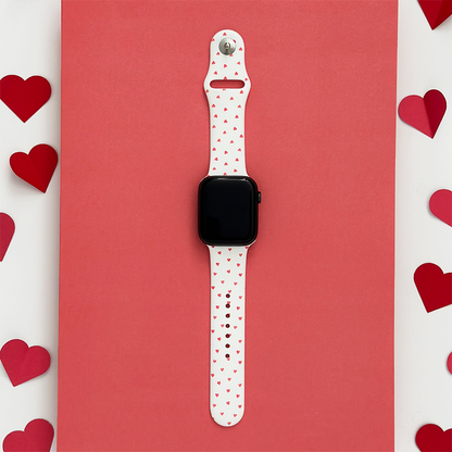 Coconut Lane Apple Watch strap with red mini hearts pattern, displayed on a red background with paper heart shapes.