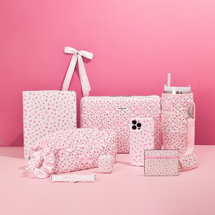 Pink Apple Watch strap with watercolor flower pattern next to pink quilted accessories on a pink background.