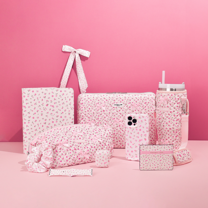 Pink Apple Watch strap with watercolor flower pattern next to pink quilted accessories on a pink background.