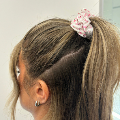 Blonde woman with ponytail wears a pink scrunchie with watercolour floral pattern, viewed from behind.