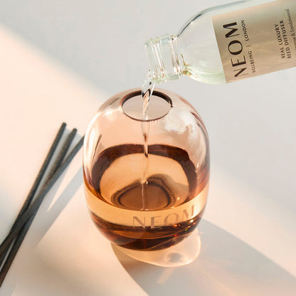 NEOM Real Luxury diffuser refill being poured into glass vessel, reusable luxury home fragrance diffuser