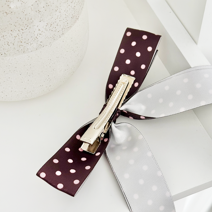 Brown polka dot ribbon bow hair clip next to a speckled container.