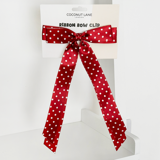 Burgundy polka dot ribbon bow hair clip on branded card, set on a white shelf.