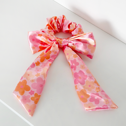 Pink satin scrunchie with bow, featuring orange and pink floral patterns.