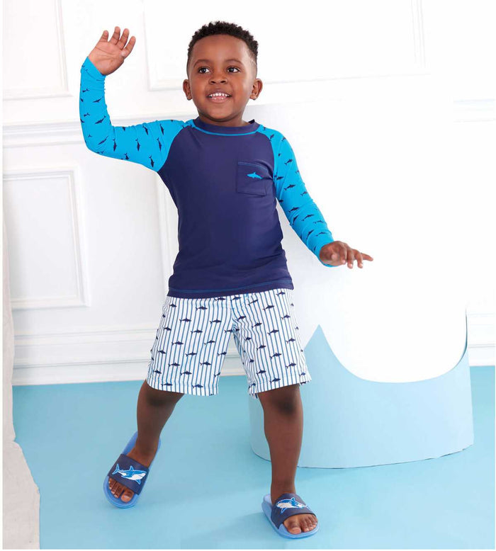 Hatley Silhouette Sharks long sleeve rashguard in navy and blue worn by boy with matching swim trunks