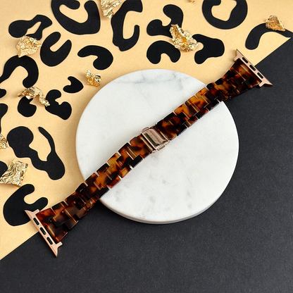 Slim luxe tortoiseshell Apple Watch strap by Coconut Lane on white marble with a black and gold animal print background.
