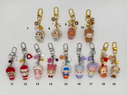 Thirteen numbered flocked-texture character keychains on a white background. Top row features soft round figures: calico cat (7), white sheep (8), pink bear (9), and brown bear (10) with gold clasps and heart charms. Bottom row features chibi dolls in costumes including red tomato hat (11), red beret (12), pink cat ears (13–14), blue & white hat (15), lavender and purple bear ears (16–17), orange fox (18), and small brown sheep (19) with silver and gold clasps.
