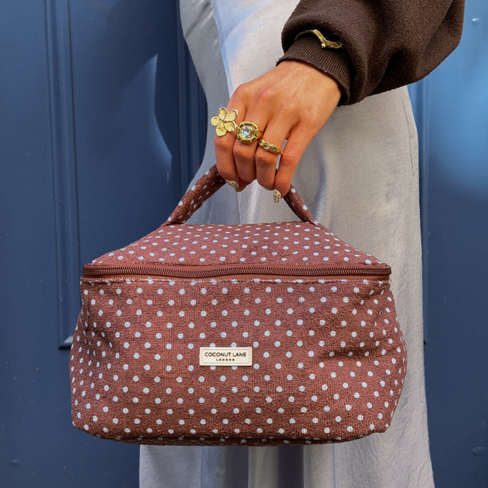 Girl by blue door holding brown and blue polka dot vanity case